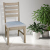 Wooden chair with a light gray cushion next to potted plants on a light wooden floor. Evy Ladderback Dining Chair available at Rustic Ranch Furniture and Decor.