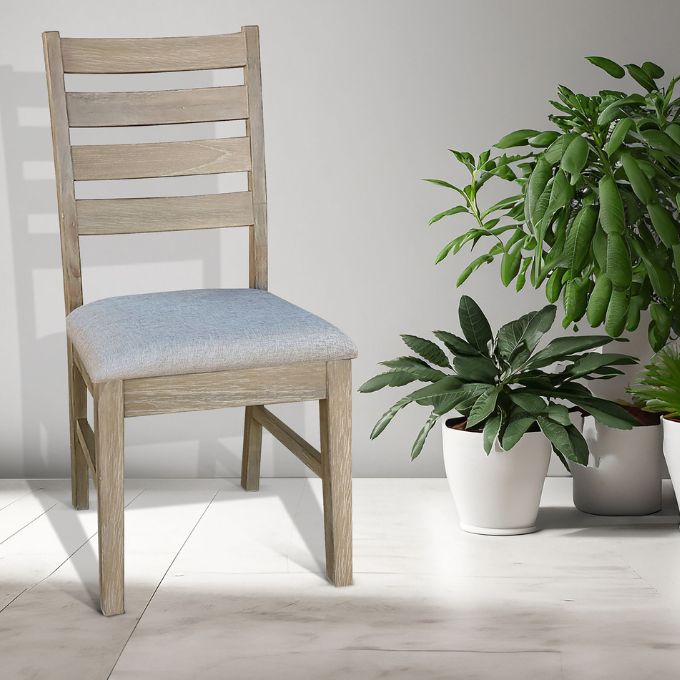 Wooden chair with a light gray cushion next to potted plants on a light wooden floor. Evy Ladderback Dining Chair available at Rustic Ranch Furniture and Decor.