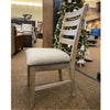 Wooden chair with a cushioned seat in a store setting with a Christmas tree in the background.  Evy Ladderback Dining Chair available at Rustic Ranch Furniture and Decor.