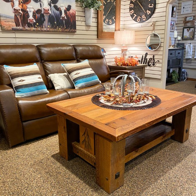 Brown leather sofa with decorative pillows in a room with wooden coffee table and decor items.   Sequoia Coffee Table available at Rustic Ranch Furniture and Decor.