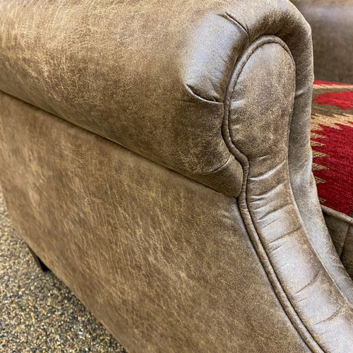 Close-up of a textured beige sofa armrest with a blurred red patterned rug in the background. Charles Chair available at Rustic Ranch Furniture and Decor.