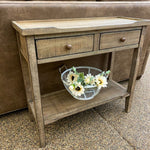 Wooden console table with two drawers and a small shelf, featuring a decorative basket of flowers. Beach Pebble Side Table available at Rustic Ranch Furniture and Decor.