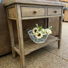 Wooden side table with a wire basket of flowers on a textured surface. Beach Pebble Side Table available at Rustic Ranch Furniture and Decor.