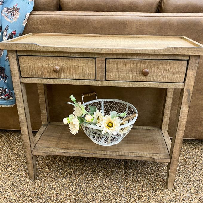 Wooden side table with two drawers and a wire basket with flowers on a carpeted floor. Beach Pebble Side Table available at Rustic Ranch Furniture and Decor.