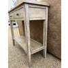 Wooden side table with a single drawer and shelf against a textured wall. Beach Pebble Side Table available at Rustic Ranch Furniture and Decor.