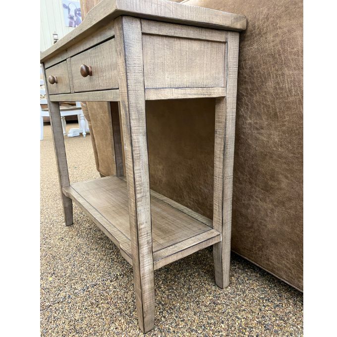 Wooden side table with a single drawer and shelf against a textured wall. Beach Pebble Side Table available at Rustic Ranch Furniture and Decor.