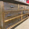 Wooden dresser with multiple drawers and metal handles on a concrete surface. Fireside Reclaimed Wood Seven Drawer Dresser available at Rustic Ranch Furniture and Decor.