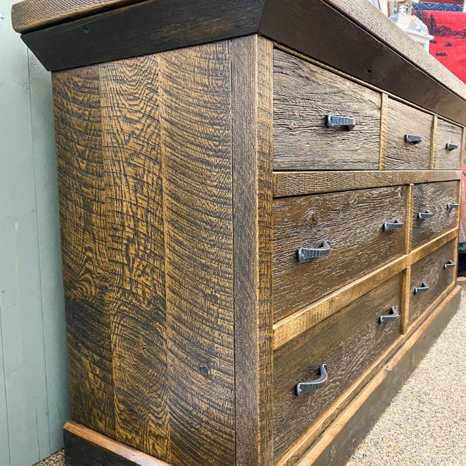 Wooden dresser with multiple drawers and metal handles on a textured surface. Fireside Reclaimed Wood Seven Drawer Dresser available at Rustic Ranch Furniture and Decor.