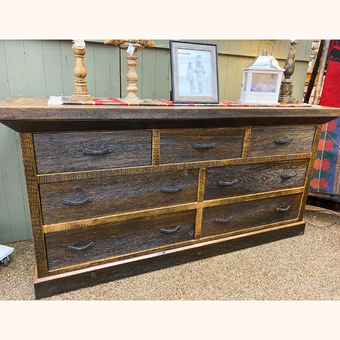 Wooden dresser with multiple drawers on a surface with decorative items in the background. Fireside Reclaimed Wood Seven Drawer Dresser available at Rustic Ranch Furniture and Decor.