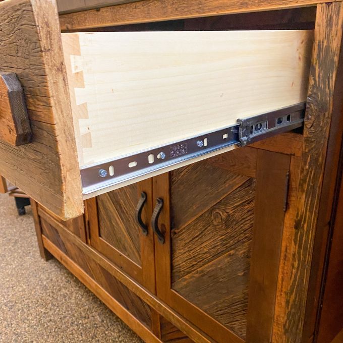 Wooden cabinet with a drawer being pulled out, showing metal slides.  Jackson Hole Four Door Sideboard available at Rustic Ranch Furniture and Decor.