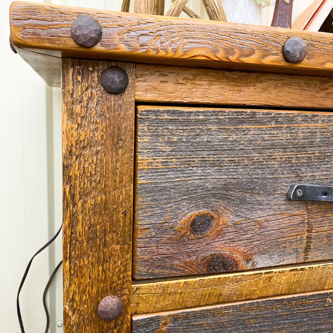 Close-up of a wooden nightstand with metal accents. Black Hills Two Drawer Nightstand available at Rustic Ranch Furniture and Decor.
