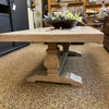 Wooden table with a pedestal base in a store setting. Gianna Coffee Table available at Rustic Ranch Furniture and Decor.