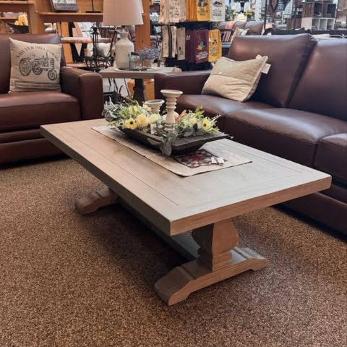Wooden coffee table with decorative items in a furniture store setting. Gianna Coffee Table available at Rustic Ranch Furniture and Decor.