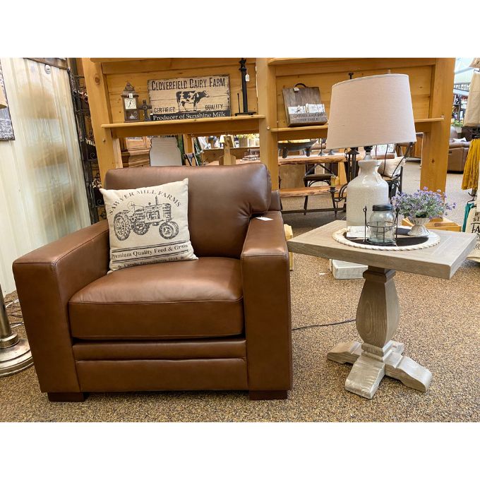 Brown leather armchair and end table with a decorative pillow in a store setting. Gianna End Table available at Rustic Ranch Furniture and Decor.
