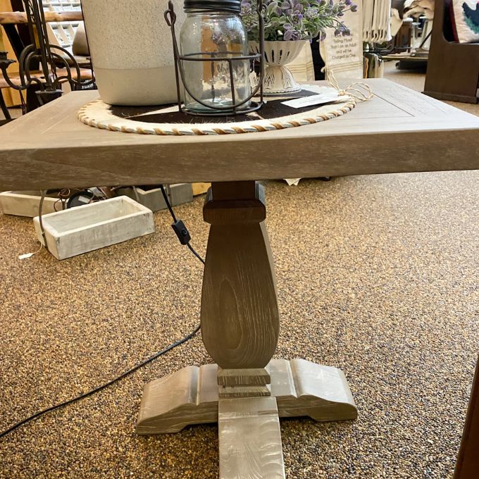Wooden table with a candle and decorative items on a carpeted floor. Gianna End Table available at Rustic Ranch Furniture and Decor.