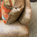 Brown leather armchair with a patterned pillow on a textured surface. Emerson Chair and a Half available at Rustic Ranch Furniture and Decor.