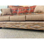 Brown sofa with decorative pillows and studded details on a textured floor.  Emerson Sofa available at Rustic Ranch Furniture and Decor.