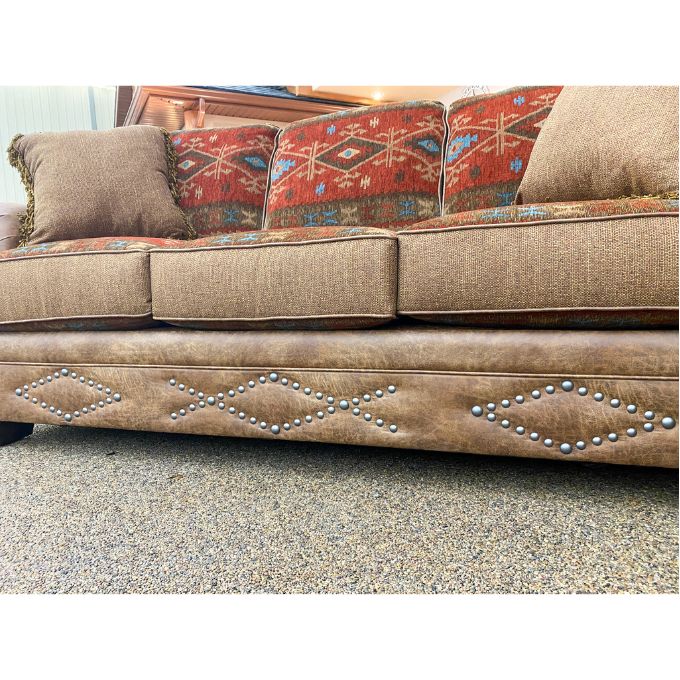 Brown sofa with decorative pillows and studded details on a textured floor.  Emerson Sofa available at Rustic Ranch Furniture and Decor.