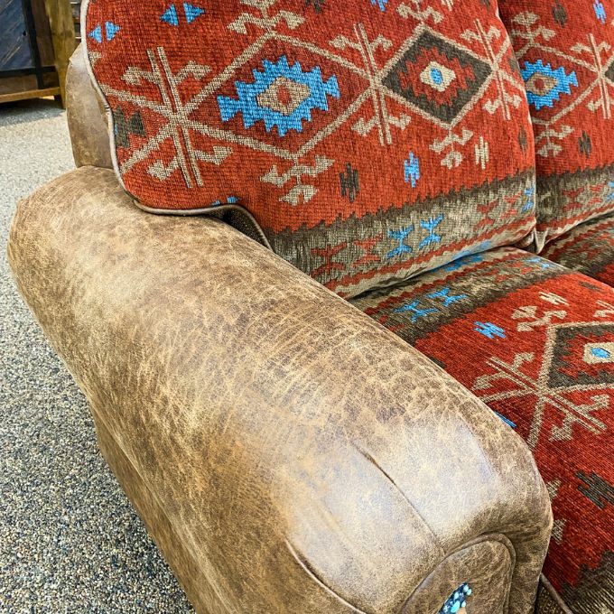 Worn-out brown chair with a patterned red cushion on a concrete floor.  Emerson Sofa available at Rustic Ranch Furniture and Decor.