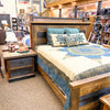 Wooden bed with bedding and pillows in a store setting. Fireside Nightstand available at Rustic Ranch Furniture and Decor.