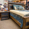 Wooden bed with bedding and pillows in a store setting. Fireside Nightstand available at Rustic Ranch Furniture and Decor.