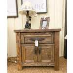 Wooden nightstand with a lamp and picture frame on top, in a room setting. Dutton Nightstand available at Rustic Ranch Furniture and Decor.