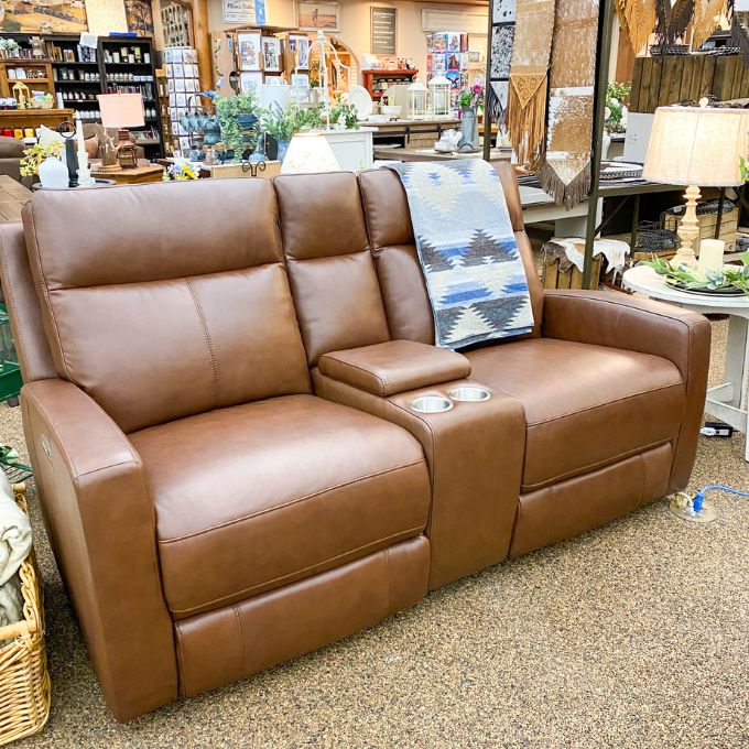 Brown leather love seat  in a store setting with various items in the background. Vienna Reclining Love Seat available at Rustic Ranch Furniture and Decor.