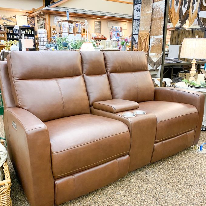 Brown leather love seat in a store setting with various items in the background.  Vienna Reclining Love Seat available at Rustic Ranch Furniture and Decor.