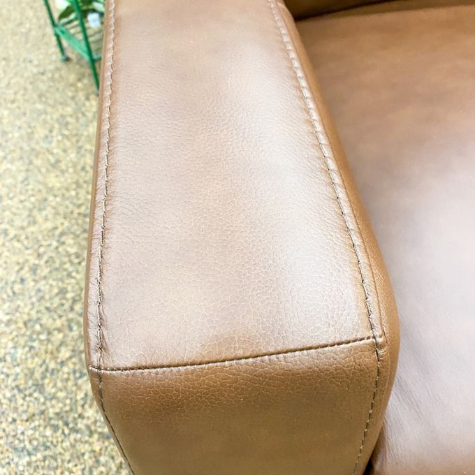 Close-up of a brown leather seat with visible stitching on a textured surface.  Vienna Reclining Love Seat available at Rustic Ranch Furniture and Decor.