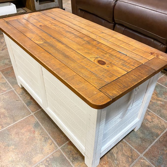 Wooden storage chest with a white base on a tiled floor. White Dashbury Storage Trunk available at Rustic Ranch Furniture and Decor.