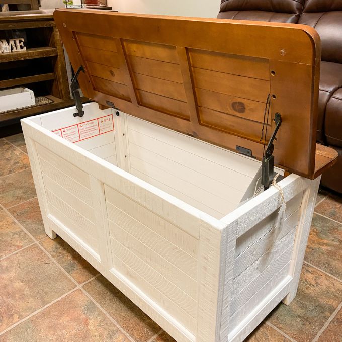 Wooden storage chest with a white interior in a living room setting. White Dashbury Storage Trunk available at Rustic Ranch Furniture and Decor.