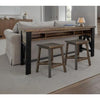 Wooden sofa table with black legs and two stools in a living room setting. Loft Brown Counter Height Sofa Table available at Rustic Ranch Furniture and Decor.